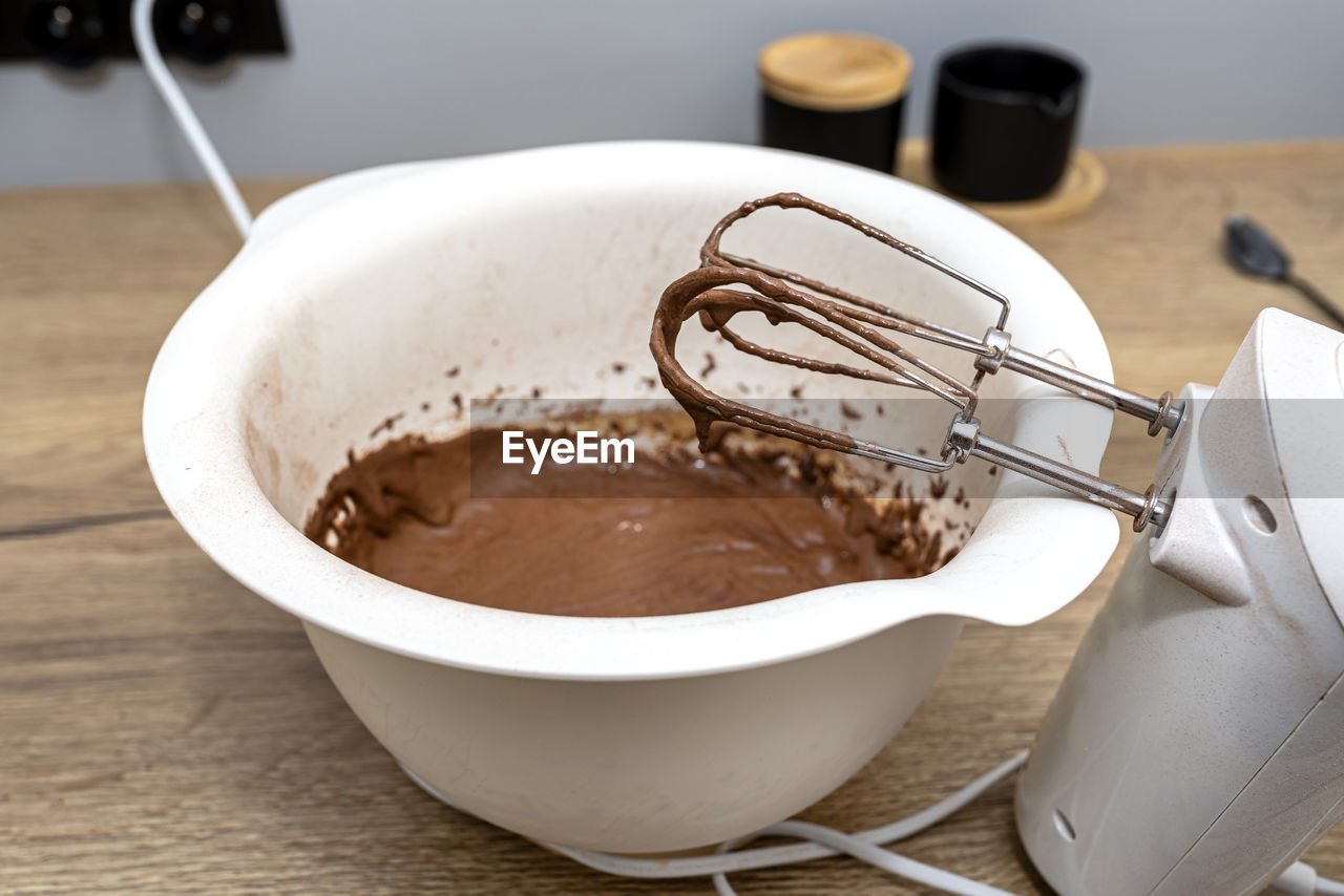 A standing hand mixer with a whisk next to the bowl, with raw dough, the dough is in a thick state.