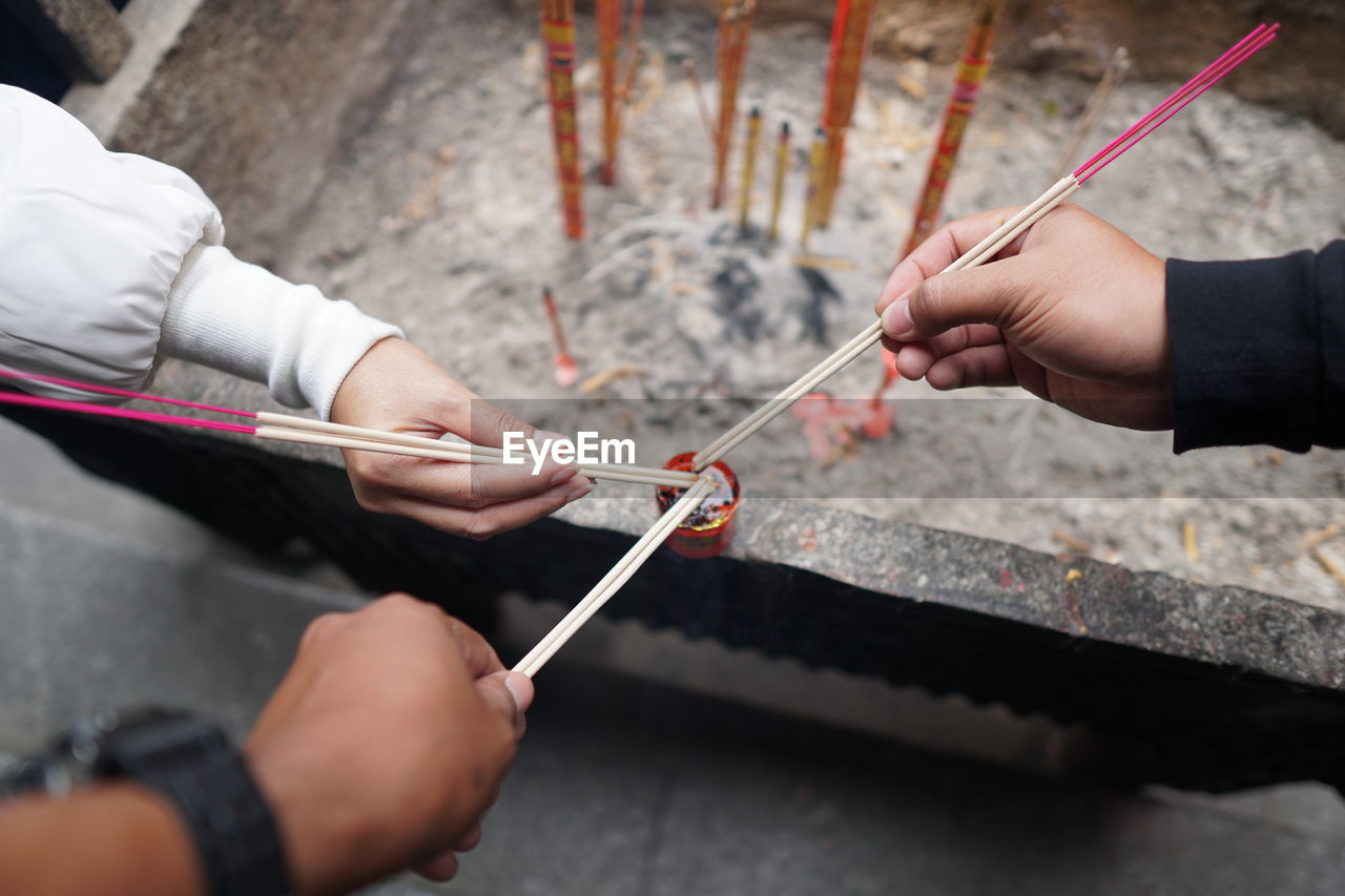 High angle view of cropped hands igniting incense sticks at temple