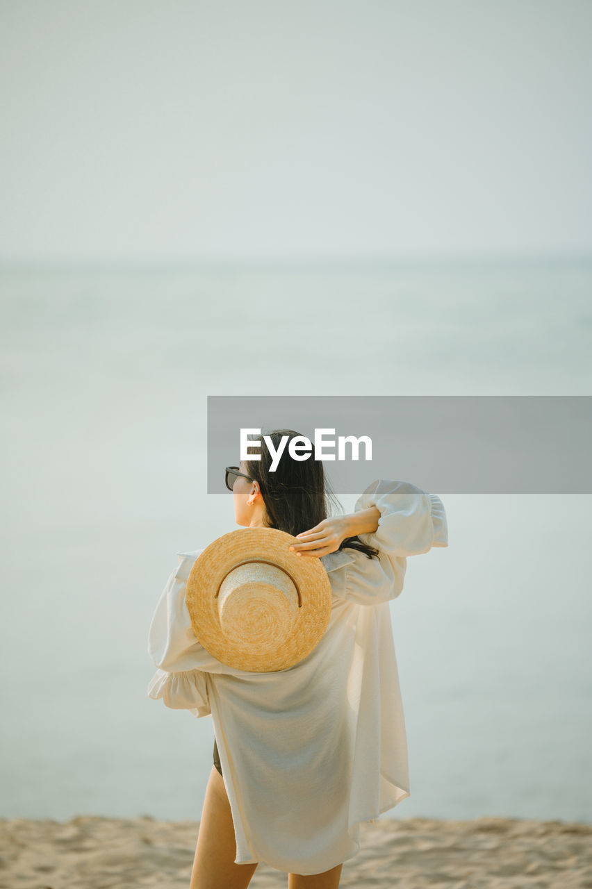 Rear view of woman holding hat standing against sea