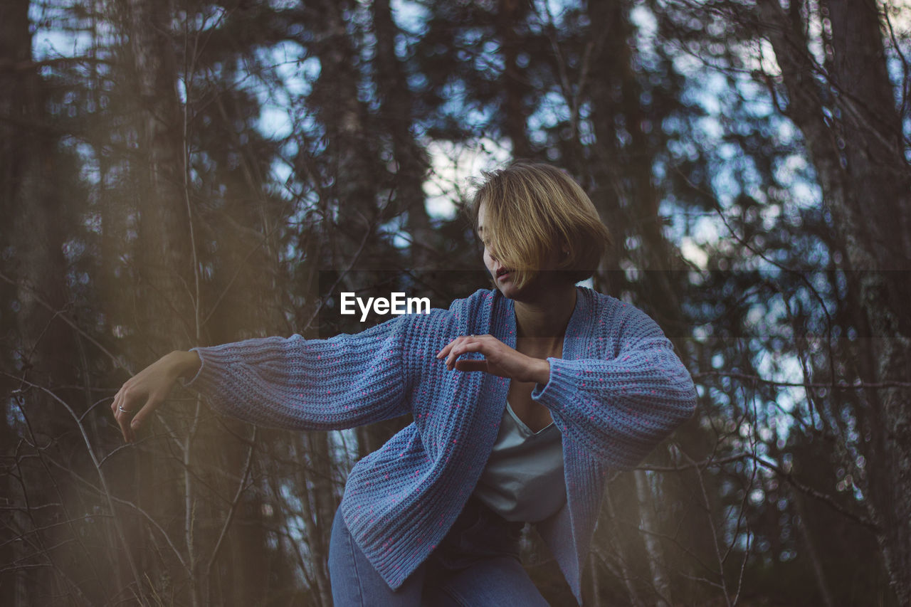 Young woman with short hair dancing against trees in forest