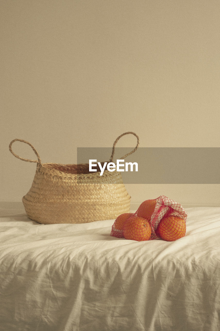 Wicker basket with oranges on bed against wall at home