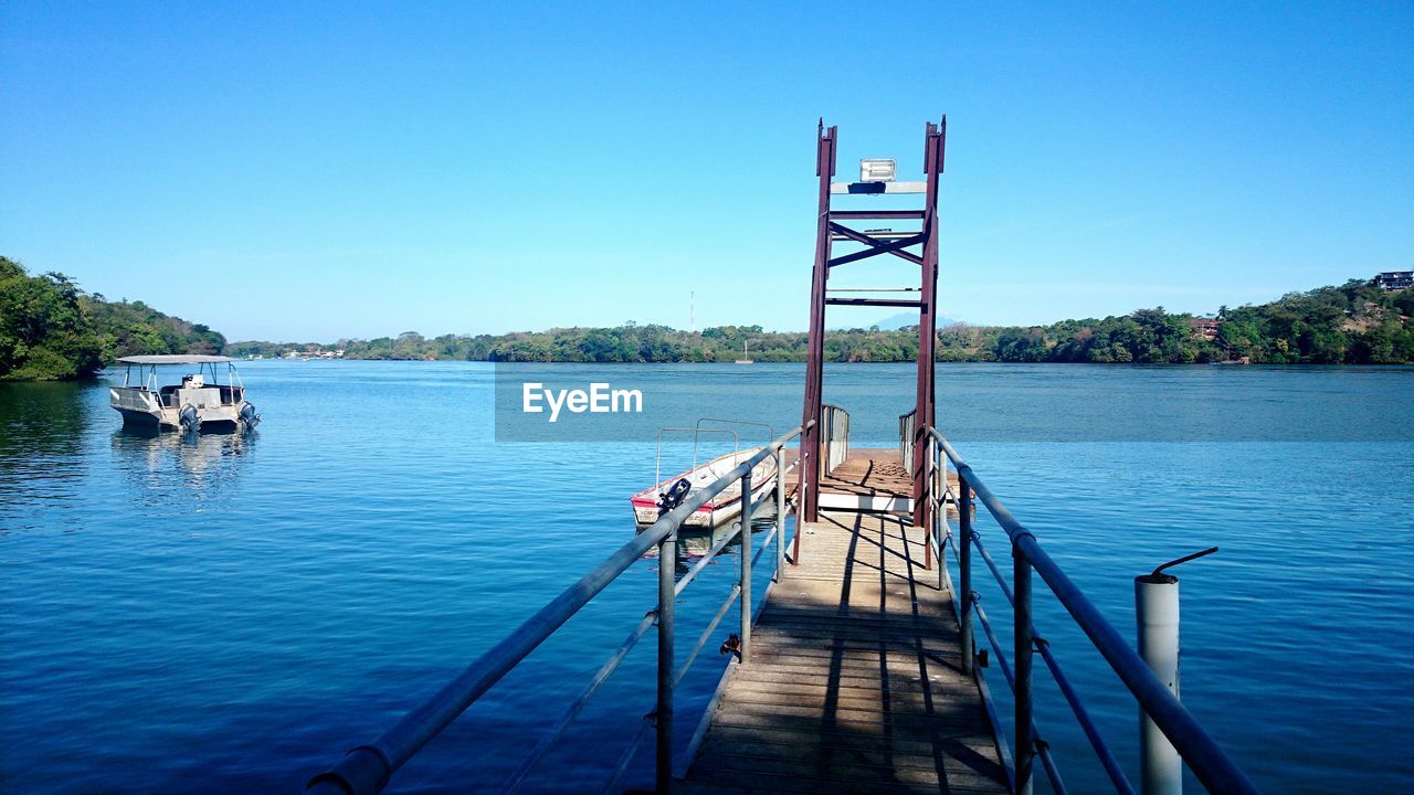 Pier amidst lake against clear blue sky