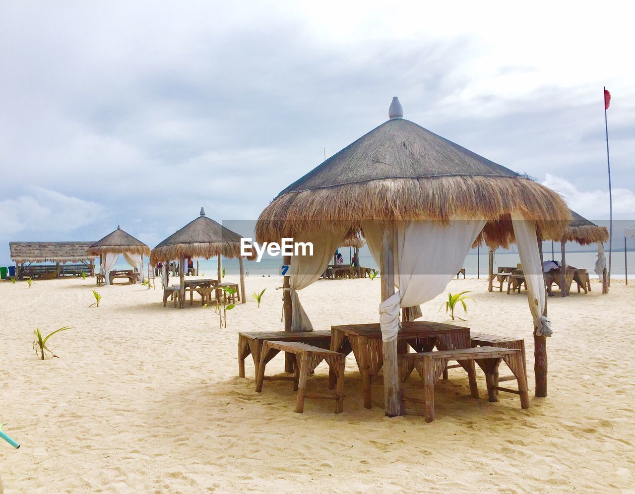 Thatched roof gazebos at beach against cloudy sky