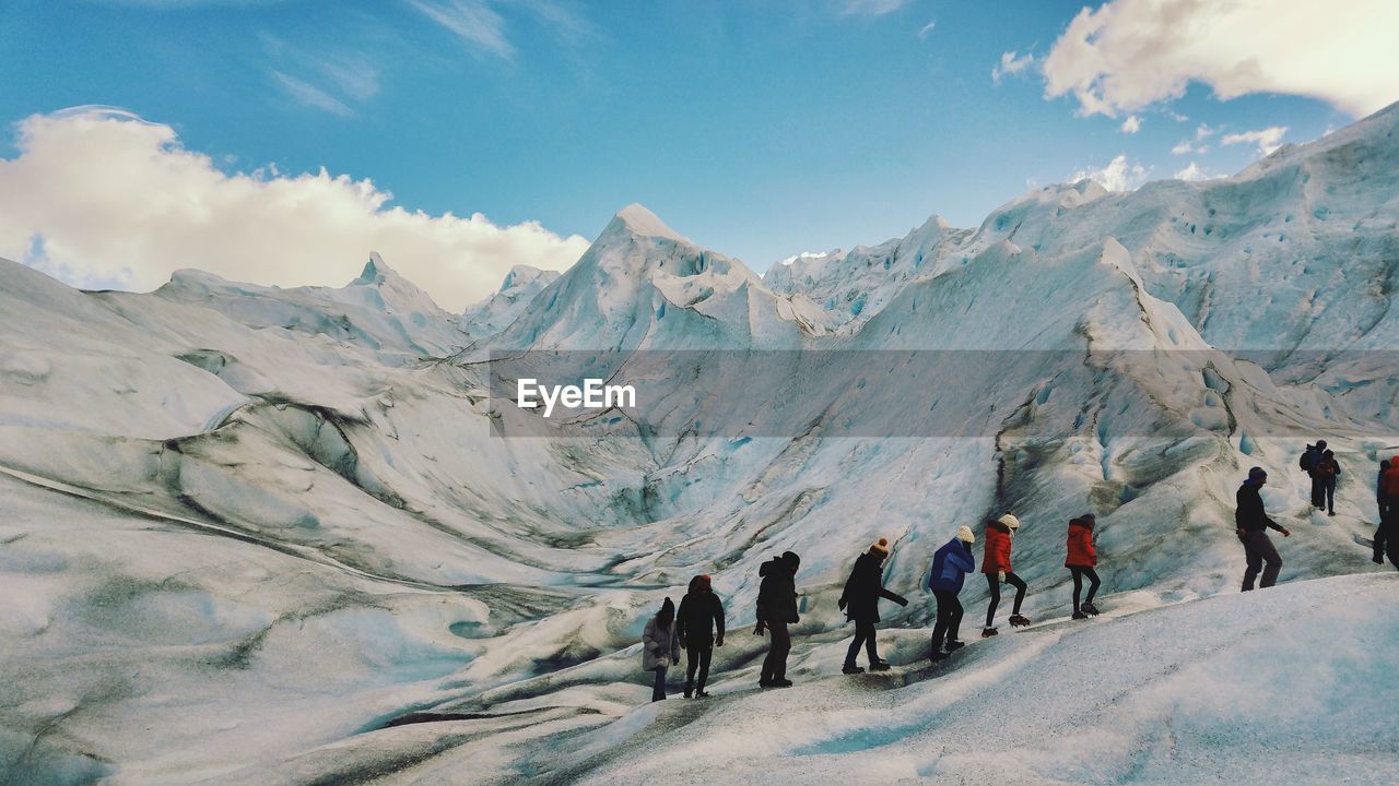 Hikers walking on snowcapped mountains against sky