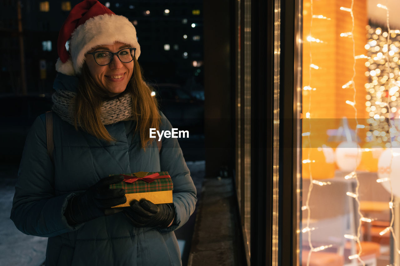 Portrait of smiling woman holding gift while standing outdoors