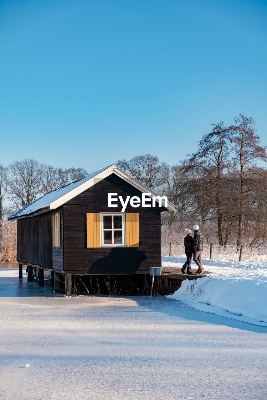 MAN WALKING ON SNOW COVERED HOUSE BY BUILDING