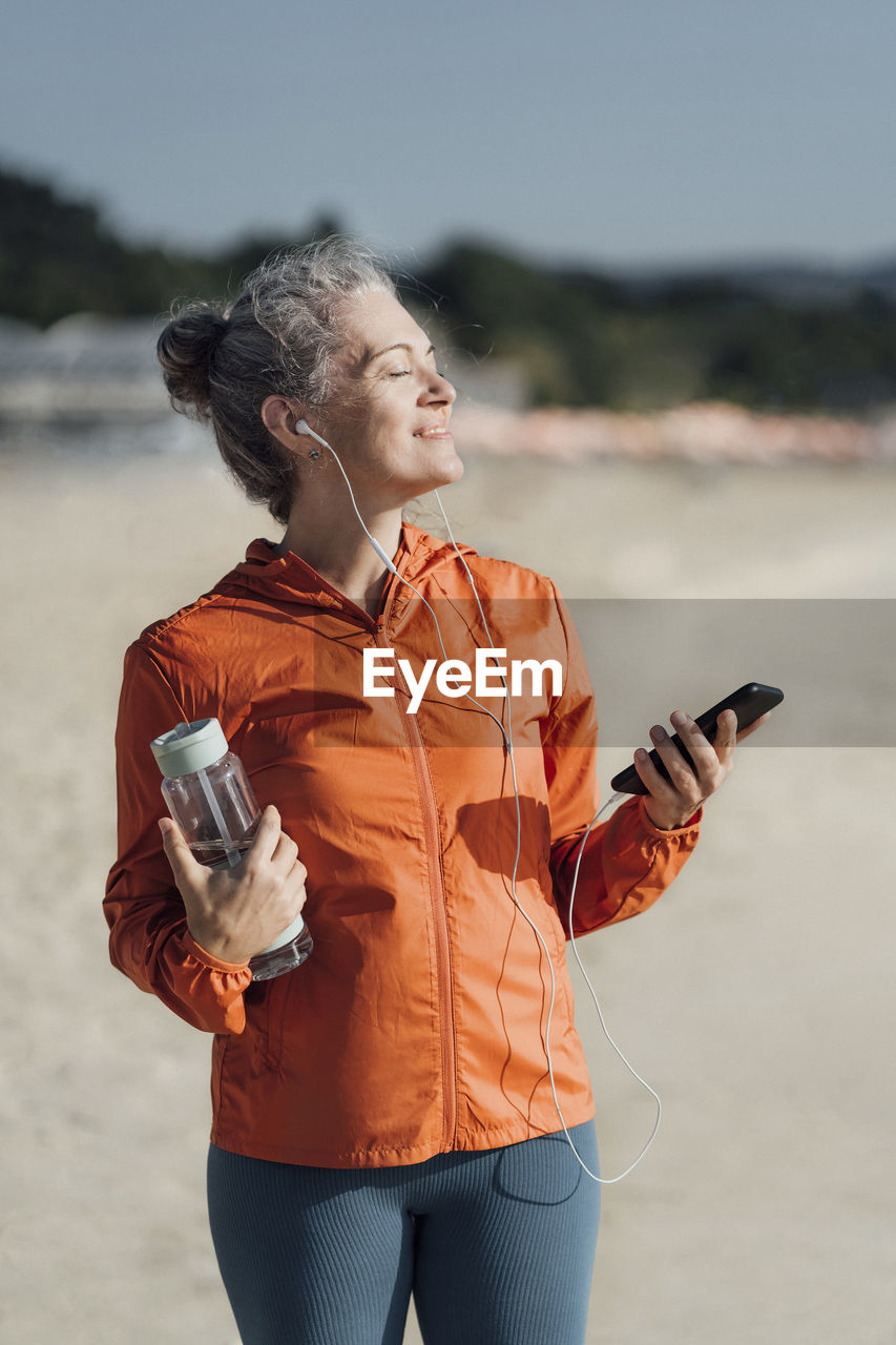 Smiling woman standing with eyes closed on beach