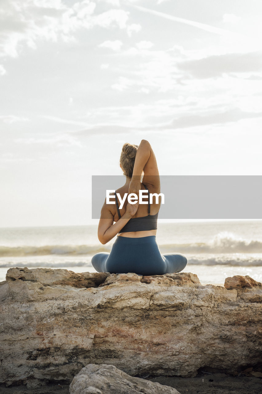 Woman doing yoga with hands behind back sitting on rock at beach