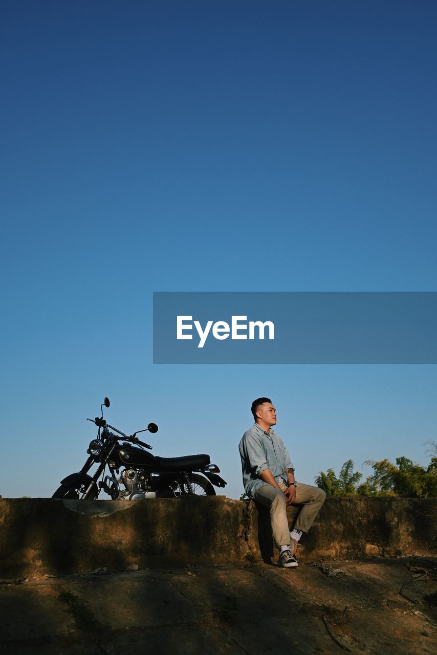 Young man sitting against blue sky