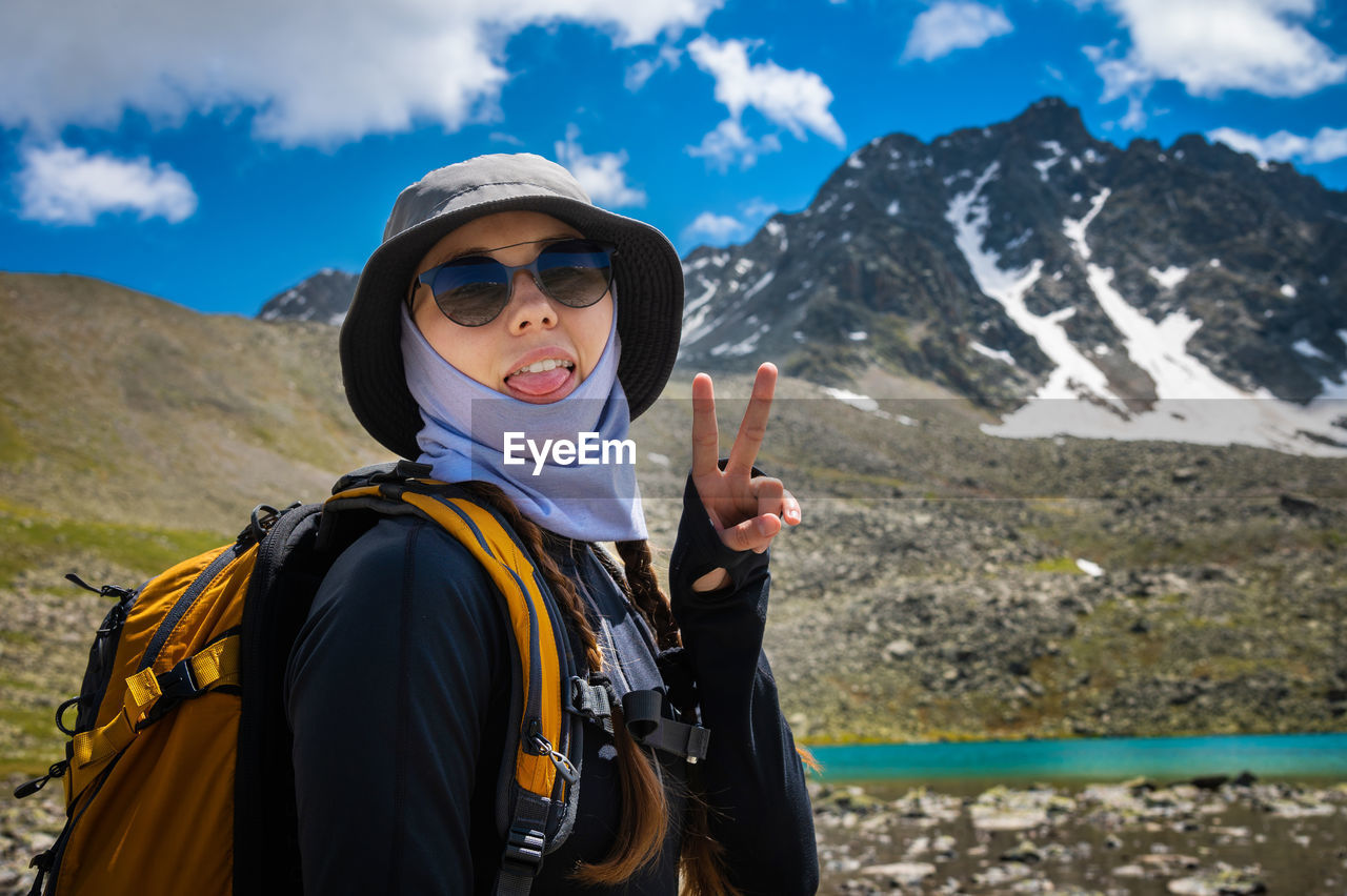 Hipster shows tongue, funny face, posing in the countryside on a sunny day, stylish hat and