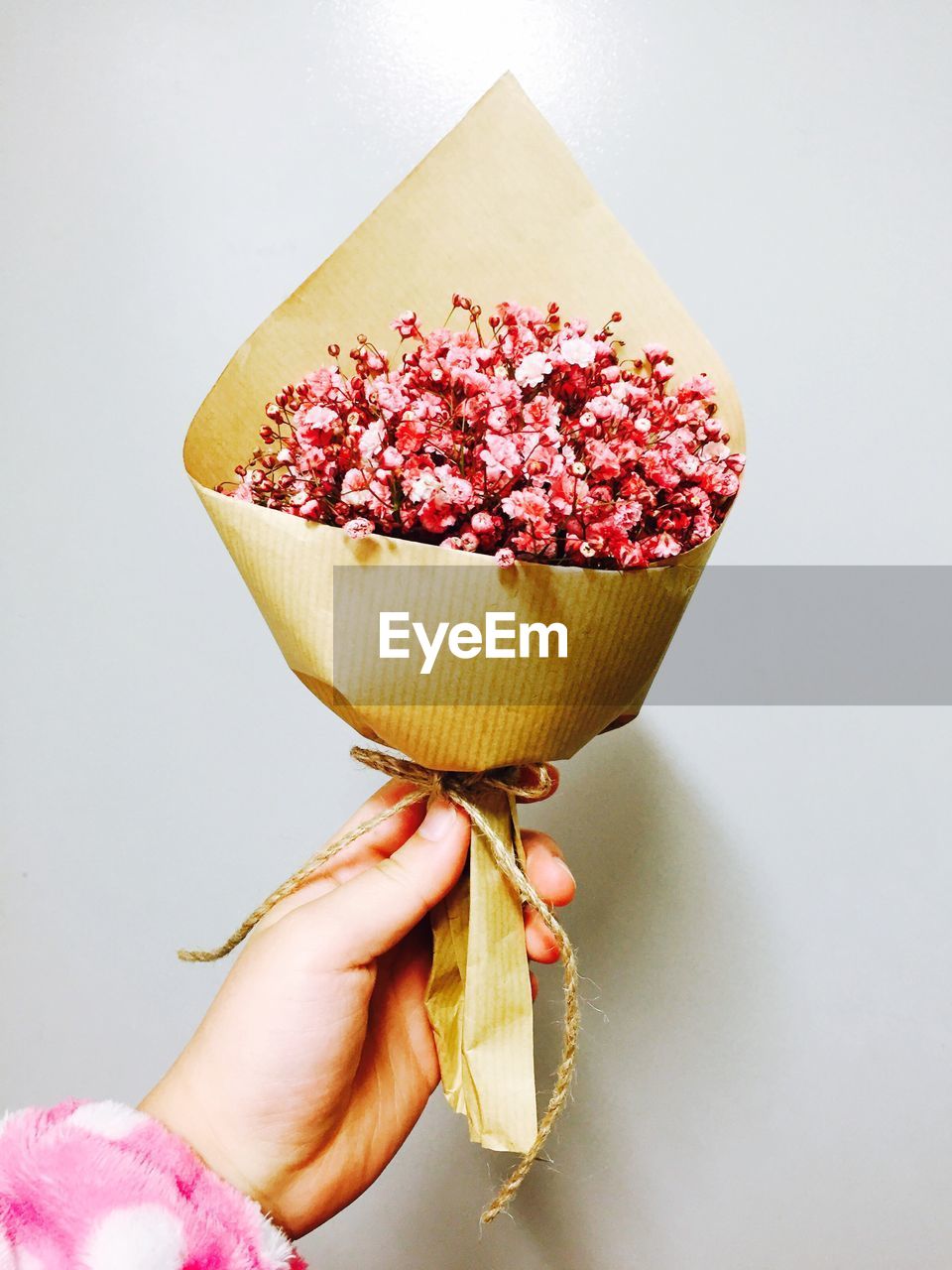 Cropped image of hand holding bouquet against gray background