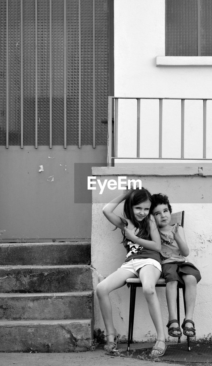 Smiling friends sitting on chair against house