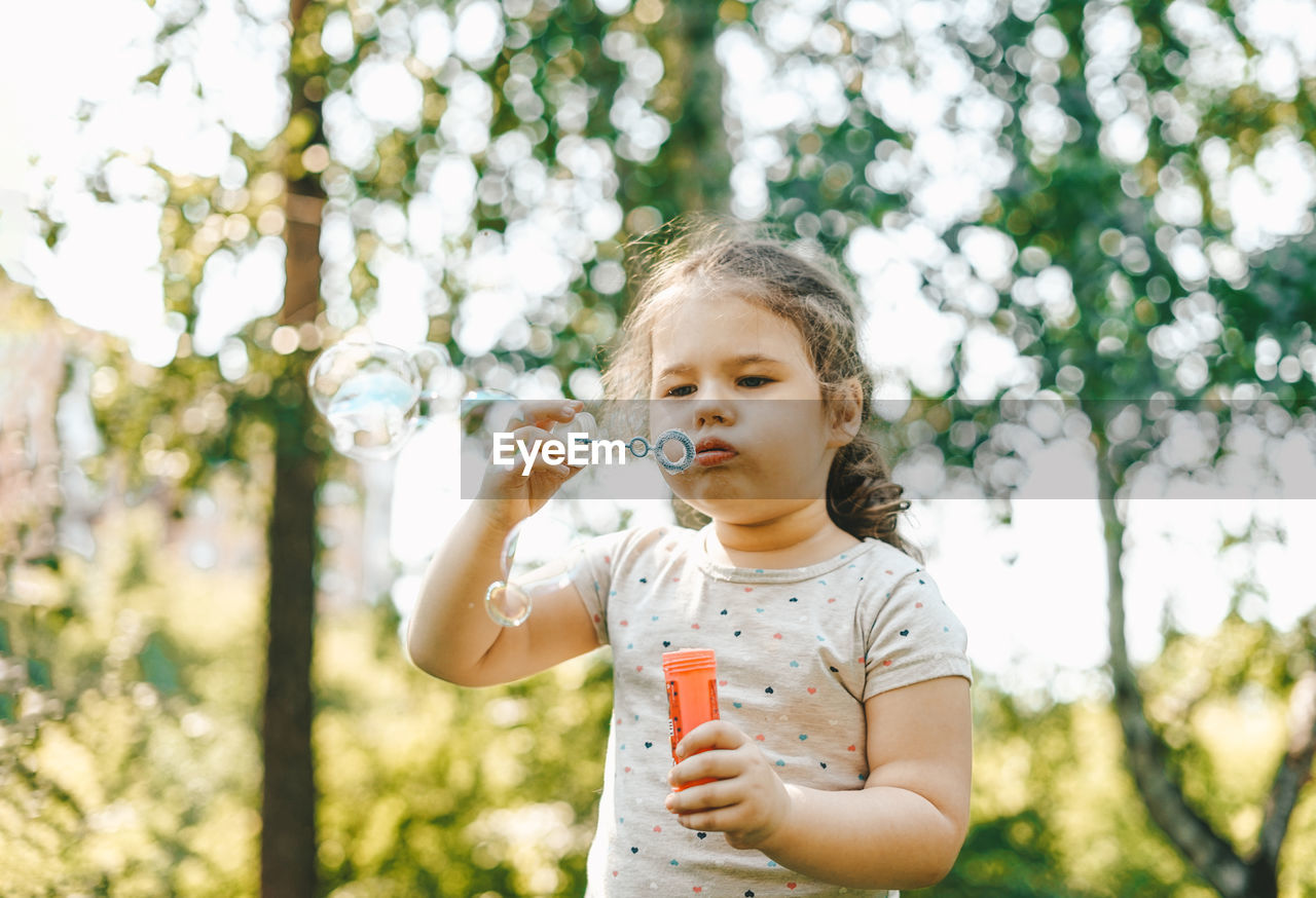 Girl blowing bubbles while standing in park