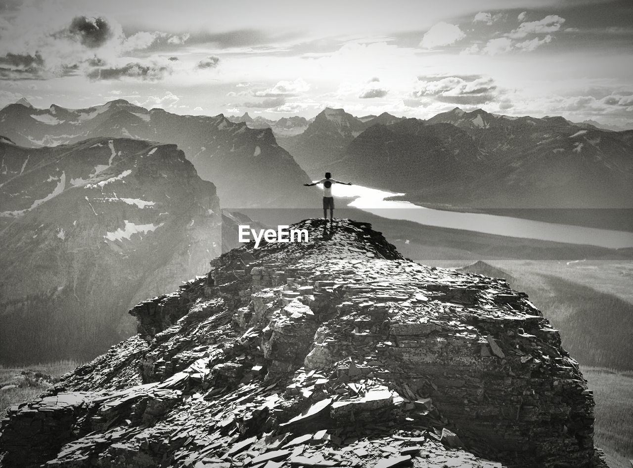 Rear view of person with arms outstretched on mountain against sky