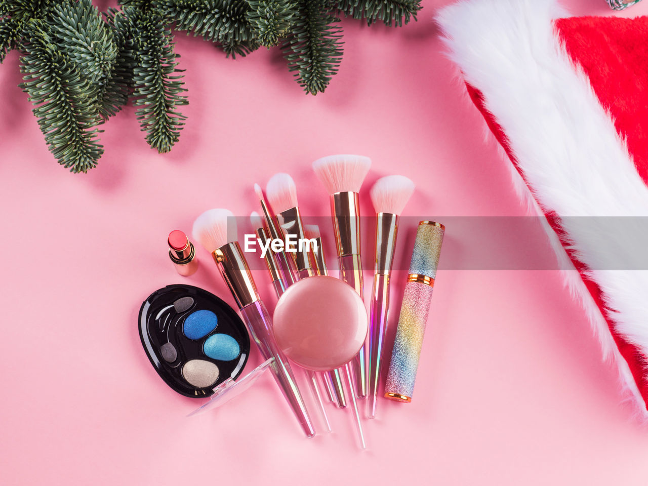 Christmas spruce branches, santa cap and presents with shiny make up tools, products on pink