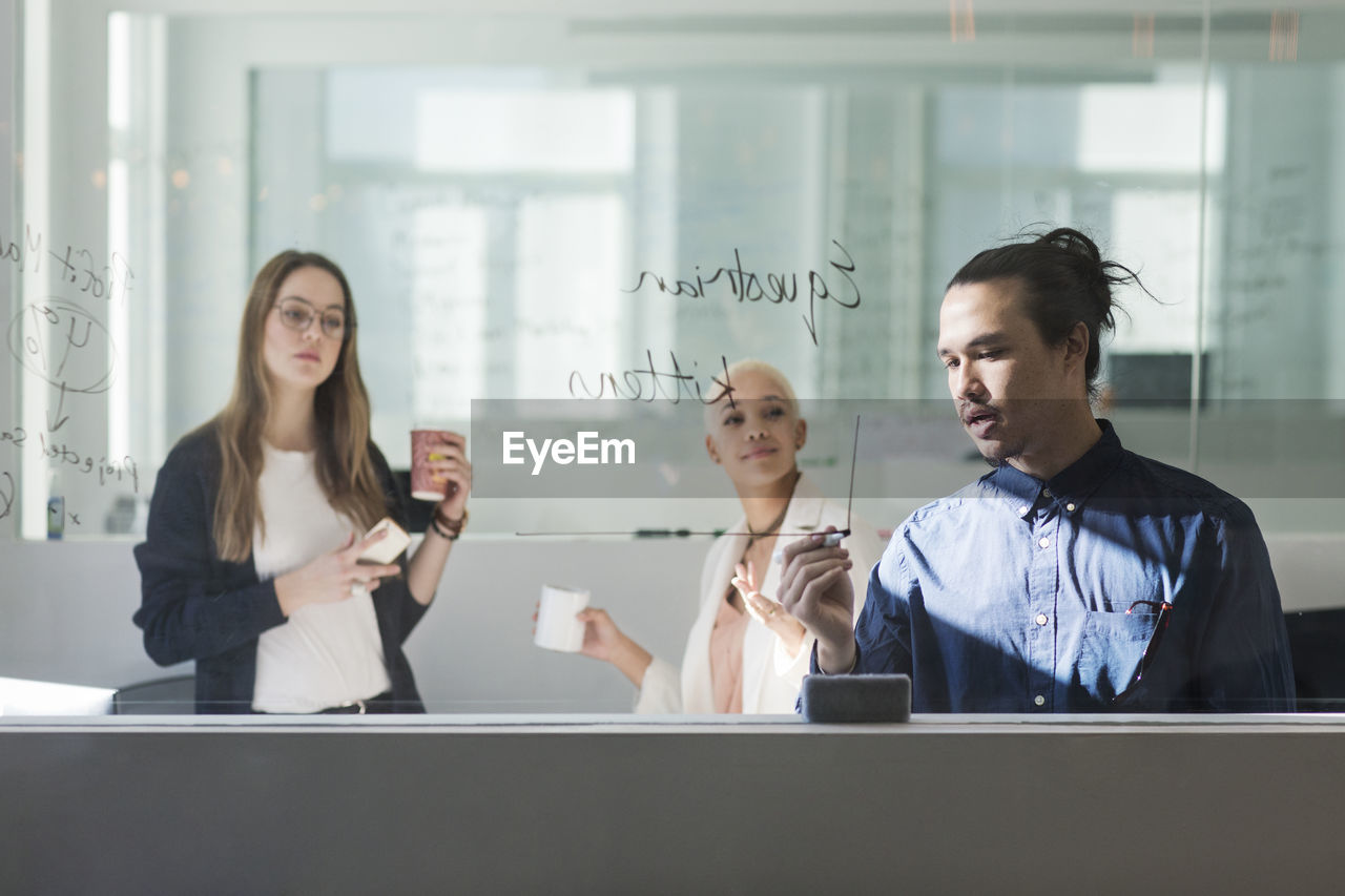 Businesswomen looking at colleague writing on window in office