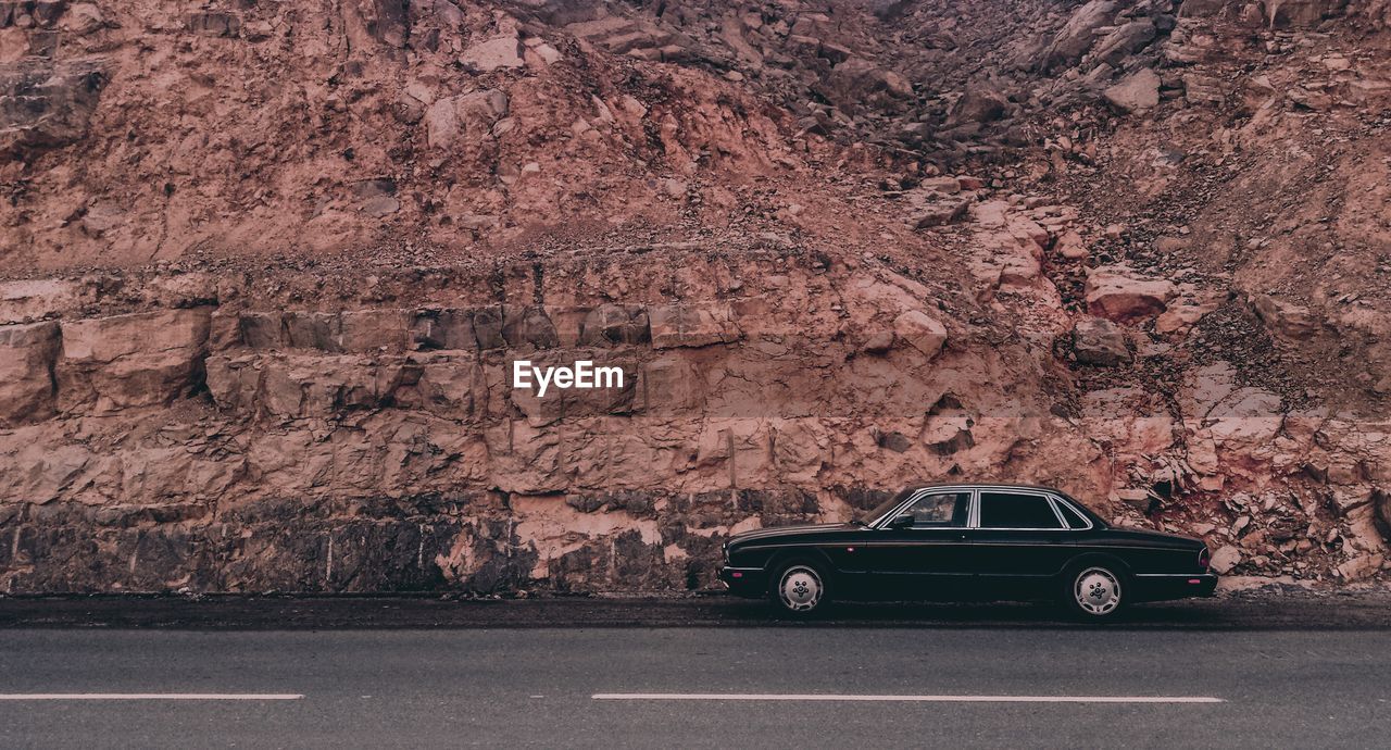 Side view of a car on road against rocky wall