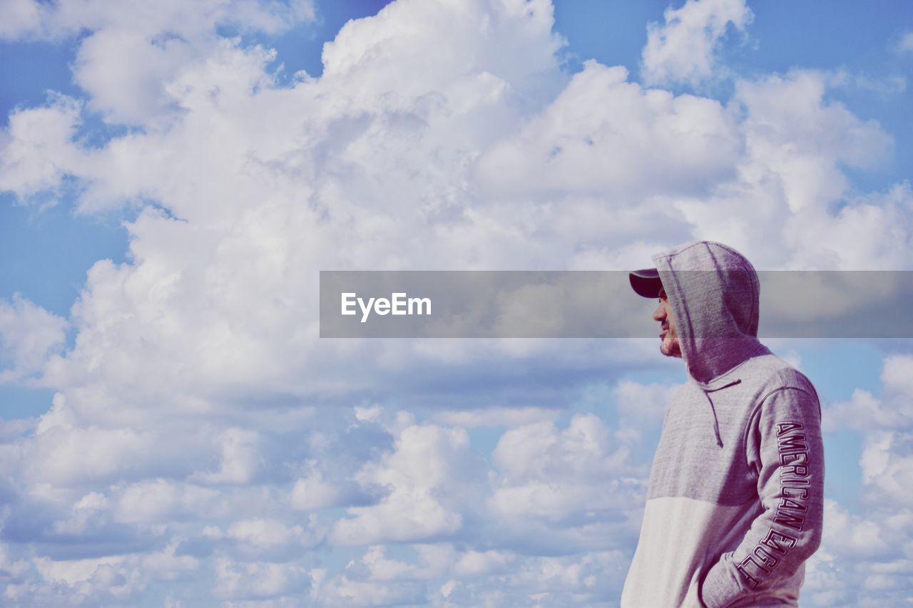 Side view of mid adult man wearing hooded shirt while against cloudy sky