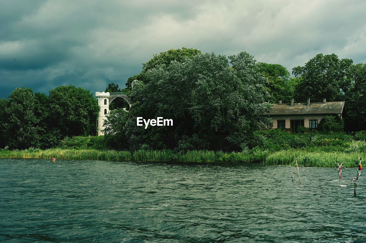 TREES IN FRONT OF BUILT STRUCTURE AGAINST CLOUDY SKY