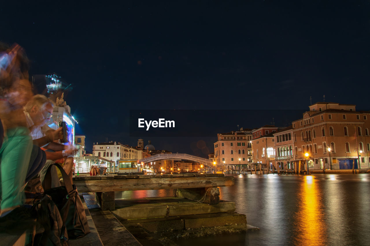 ILLUMINATED CITY BY RIVER AGAINST SKY