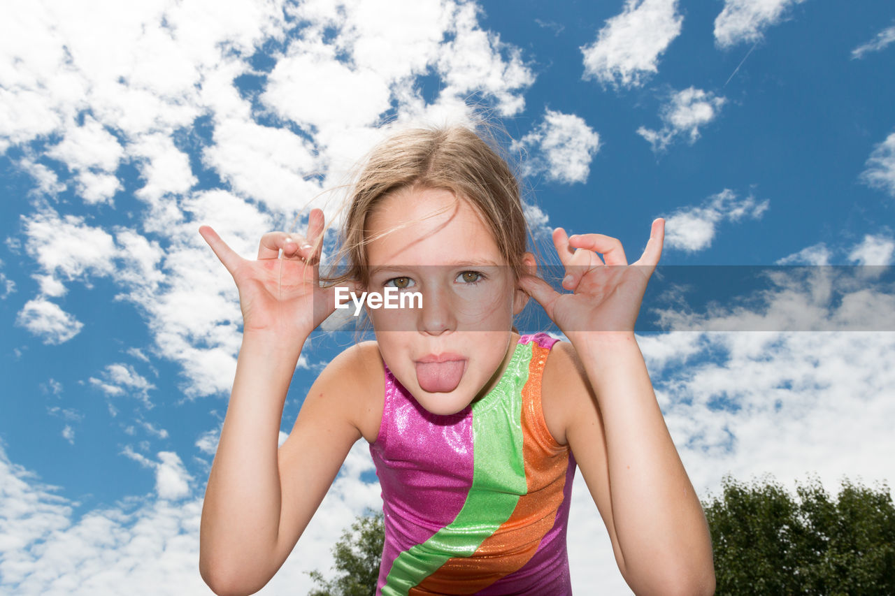 Portrait of happy girl sticking out tongue against sky