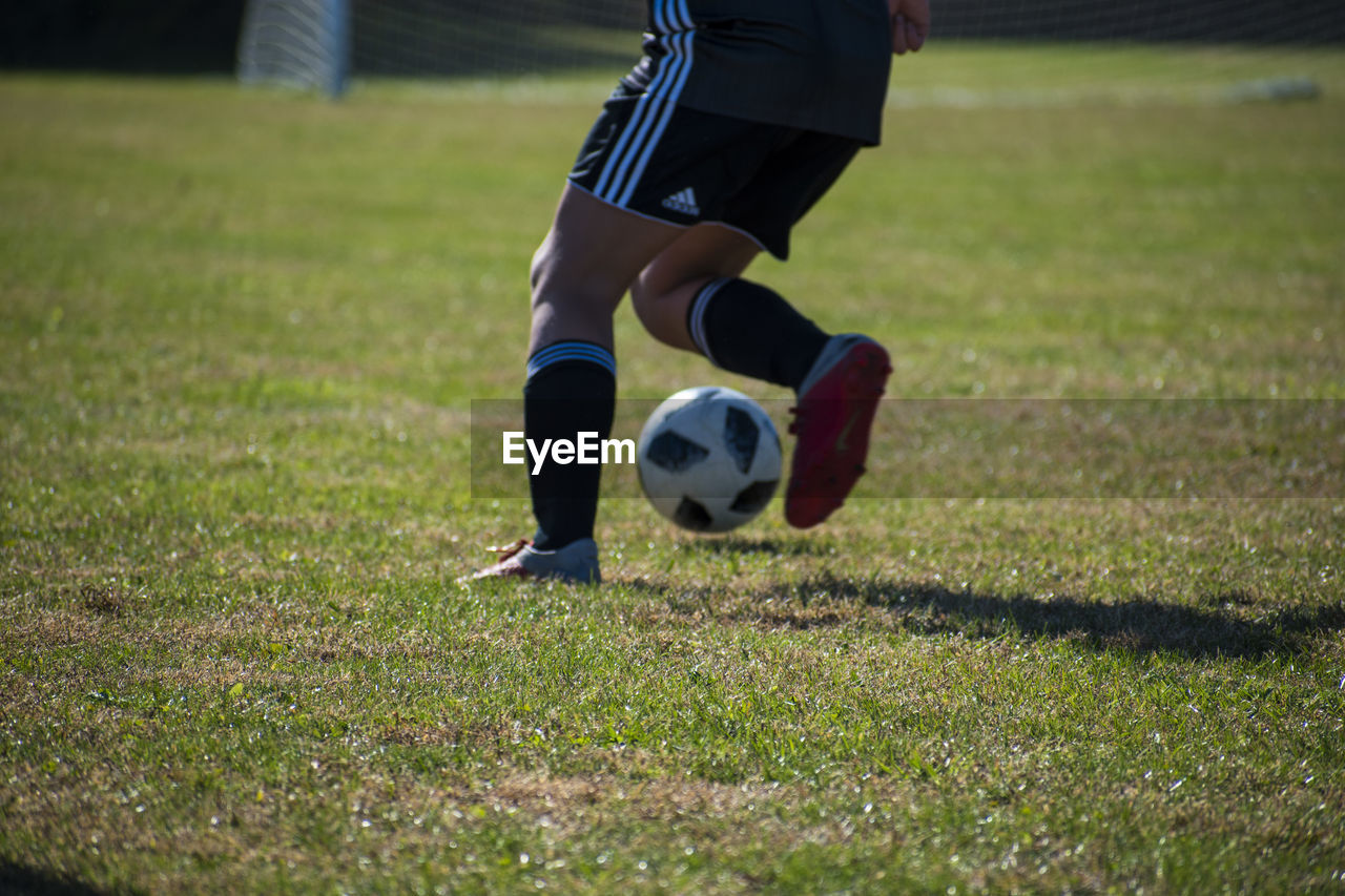 LOW SECTION OF WOMAN PLAYING SOCCER ON FIELD