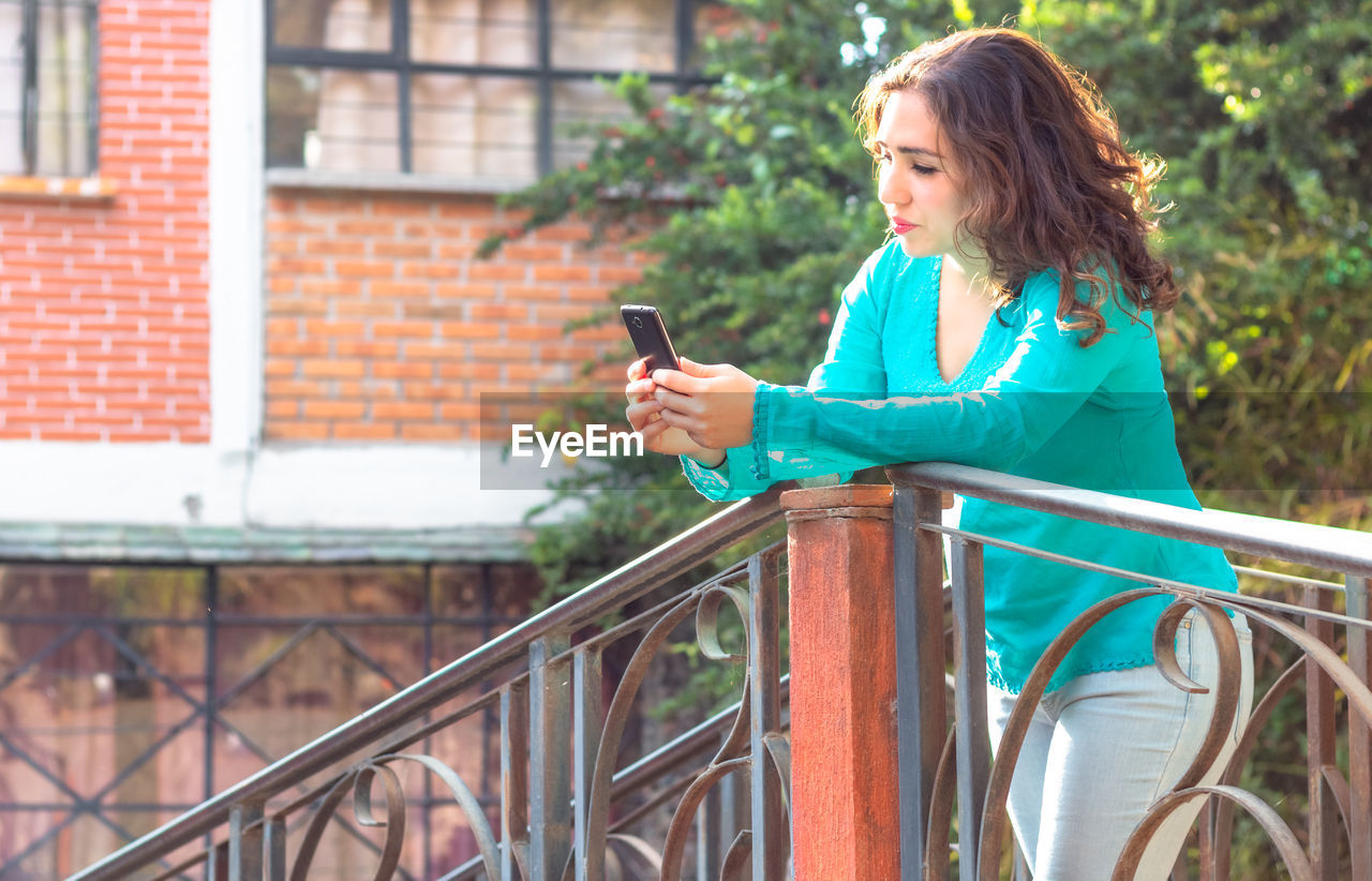 Woman using mobile phone while standing at railing