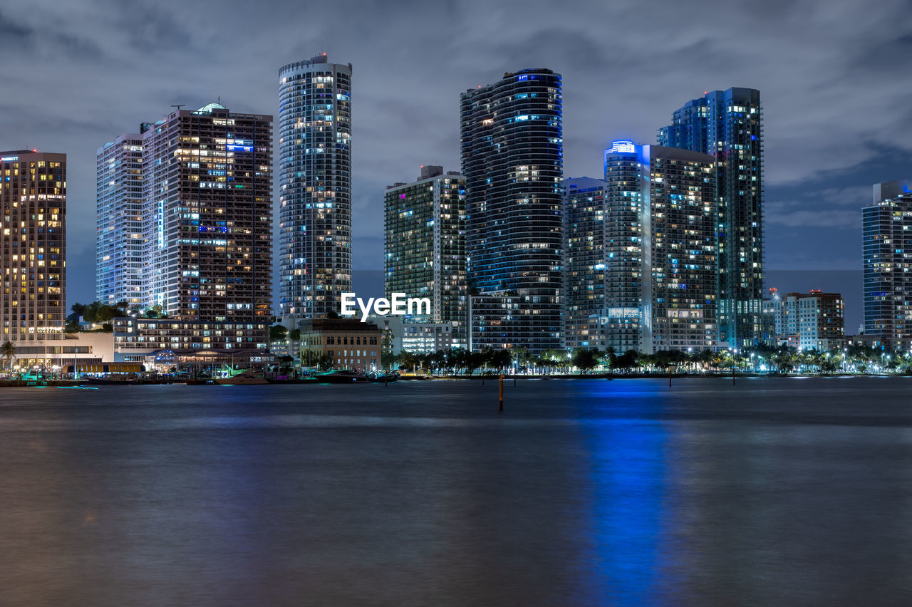 Illuminated modern buildings in city against sky at night