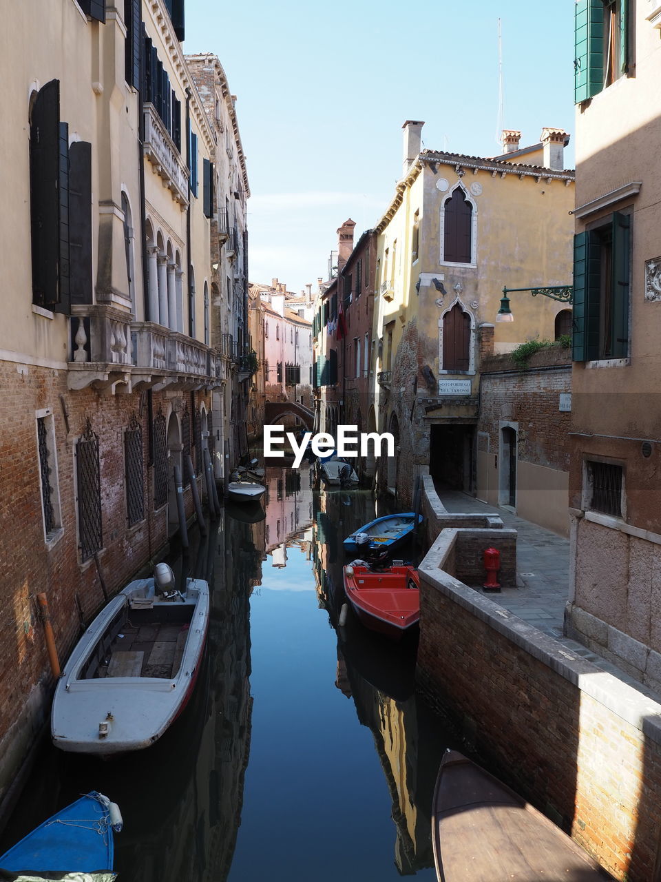 BOATS MOORED IN CANAL BY BUILDINGS AGAINST SKY