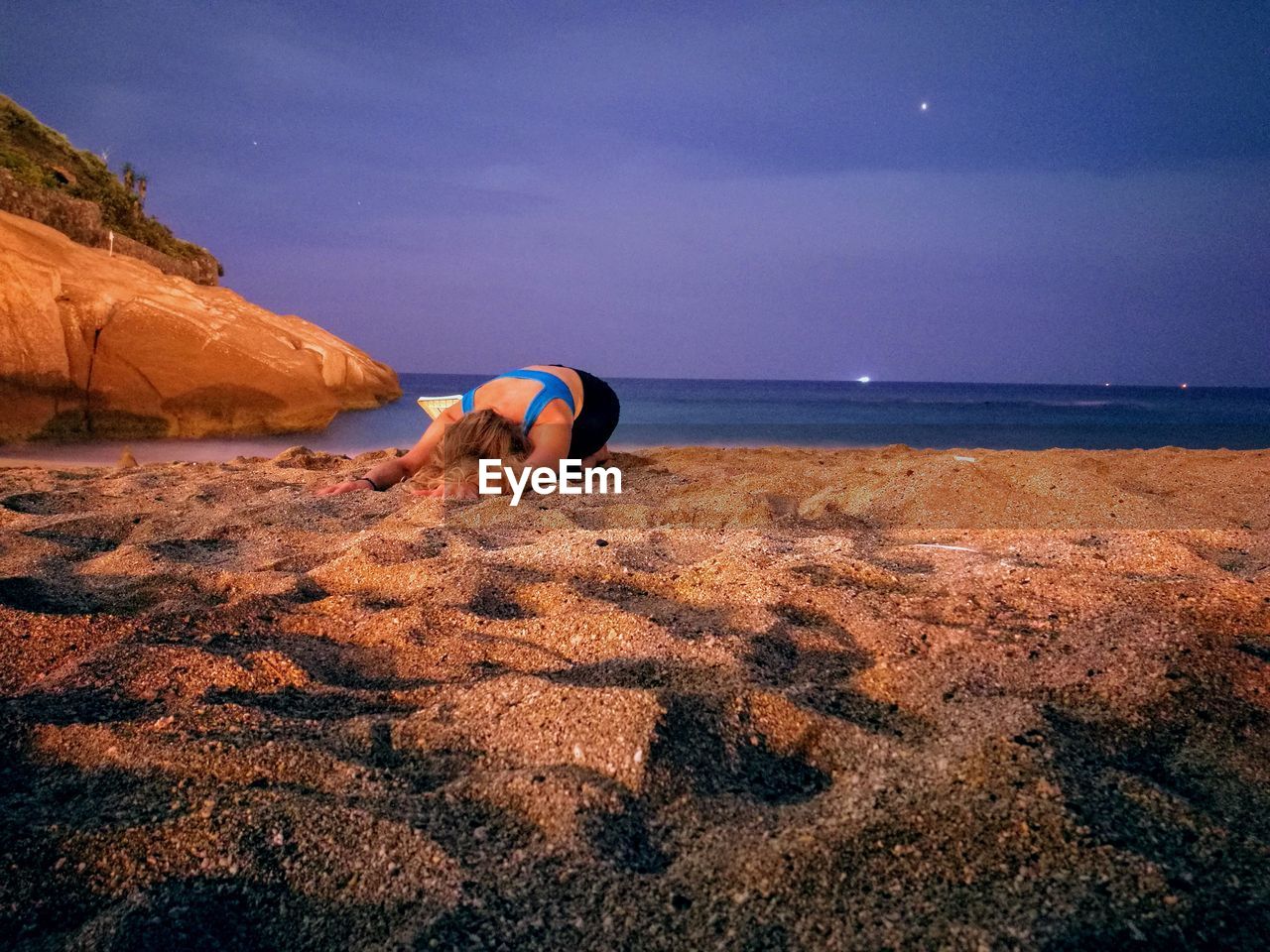 MAN RELAXING ON ROCK AT SHORE AGAINST SKY