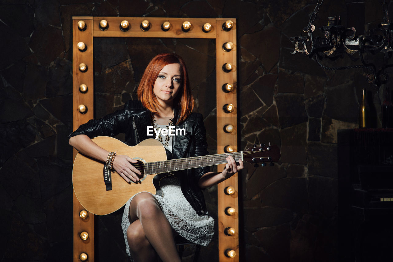 FULL LENGTH PORTRAIT OF YOUNG WOMAN PLAYING GUITAR AT MUSIC CONCERT