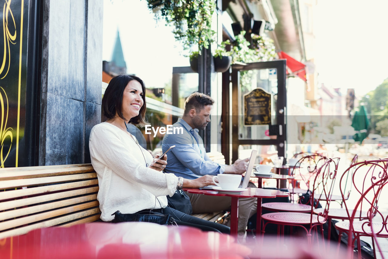 Thoughtful businesswoman holding smart phone while sitting at sidewalk cafe