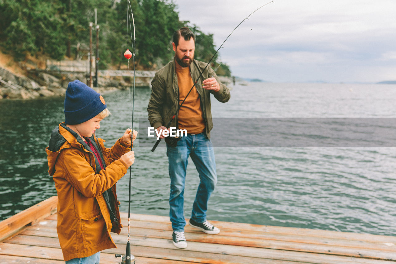 Father and son holding fishing rods while standing by sea