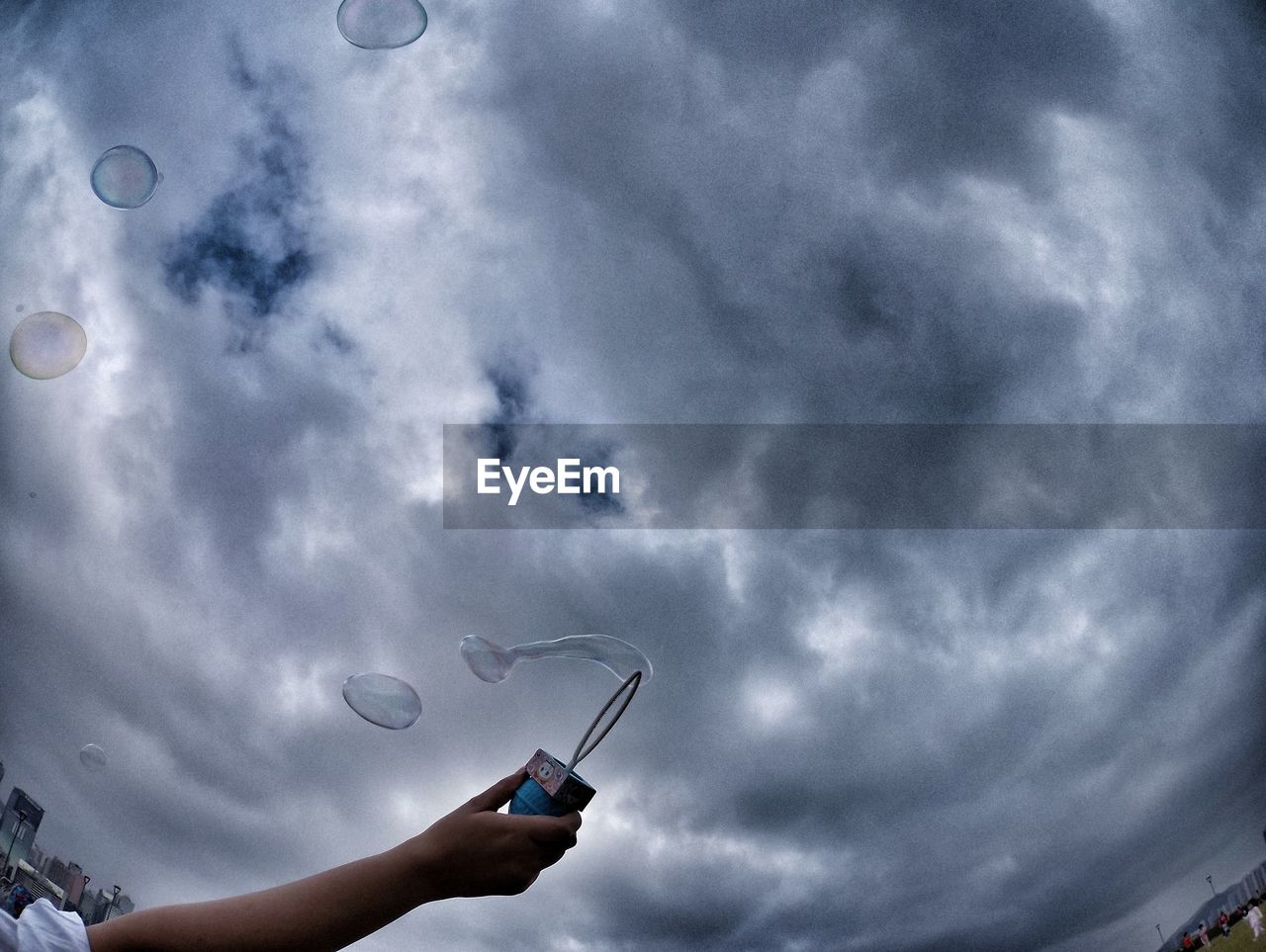 Little planet format of person holding bubble wand against cloudy sky