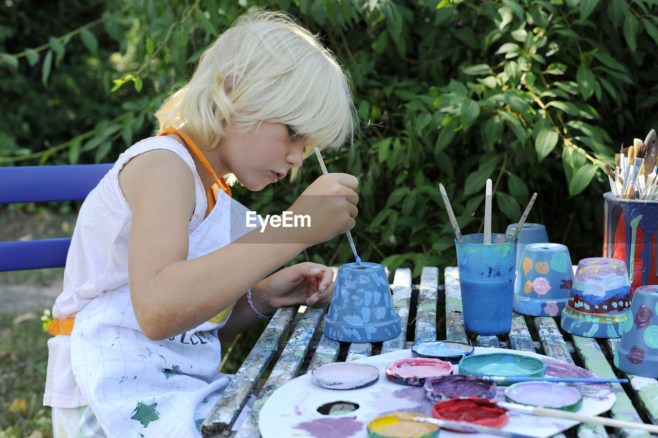 Little girl painting flower pots in garden