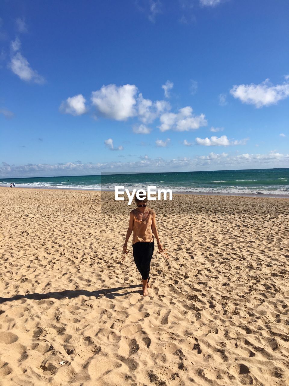 Full length of woman walking at beach against blue sky