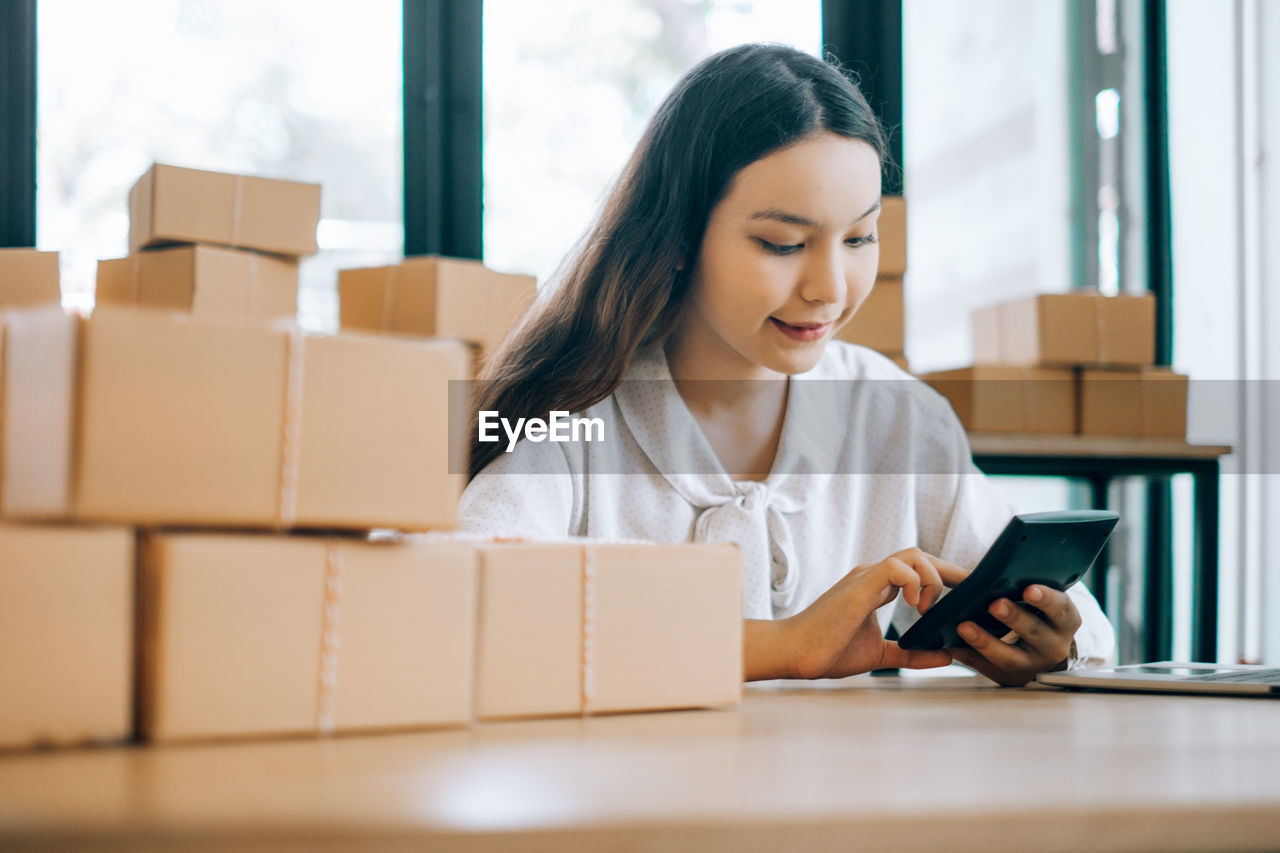 Young businesswoman working while sitting by packages at office