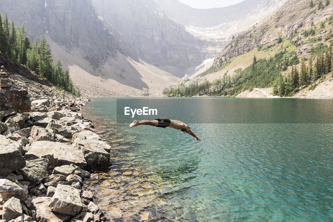 Side view of man diving in lake against mountains at banff national park