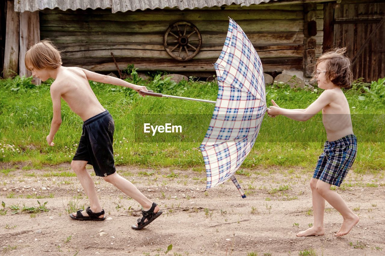 Side view of brothers holding umbrella while running on land