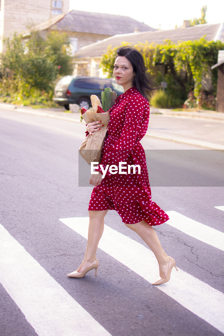 women, city, one person, pattern, pink, adult, transportation, road, fashion, young adult, dress, street, architecture, full length, polka dot, clothing, crosswalk, smiling, red, road marking, city life, hairstyle, happiness, zebra crossing, long hair, symbol, portrait, crossing, day, maroon, city street, casual clothing, walking, emotion, lifestyles, outdoors, standing, nature, brown hair, cheerful, female, summer, side view, sunlight, high heels, looking, person, spring, motion, marking, on the move, communication, teeth, car, leisure activity, carefree, smile, mode of transportation, travel, looking at camera, motor vehicle, enjoyment, building exterior, footpath