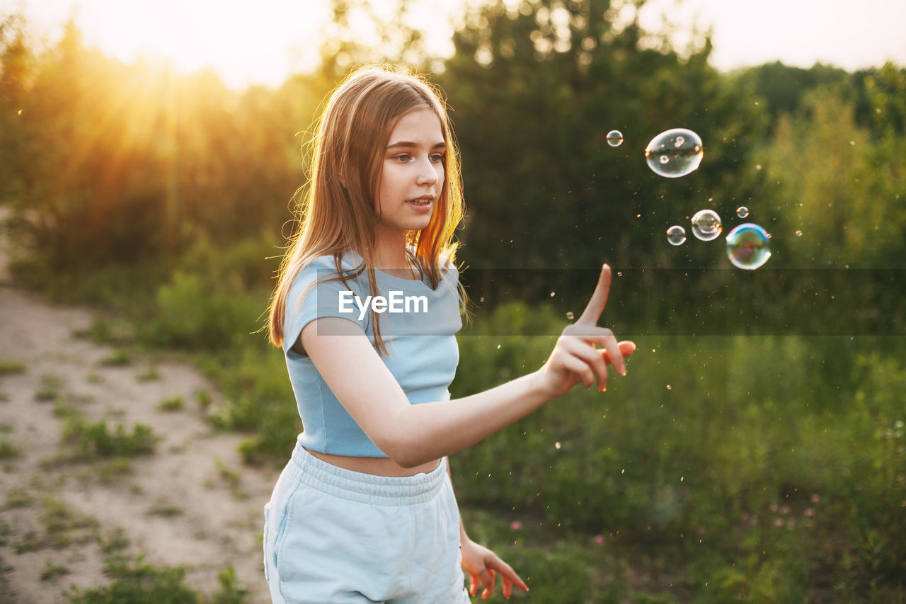 Cute girl with a beautiful smile catches soap bubbles on the background of a beautiful sunset