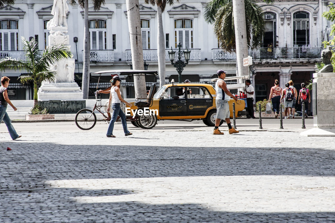 People and vehicles on road against buildings during sunny day