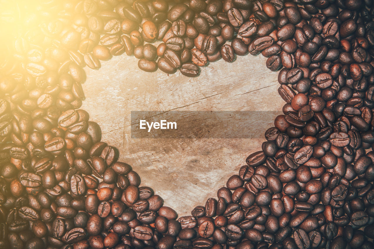 A large number of coffee beans are placed on an old wooden plate with a heart shaped space 