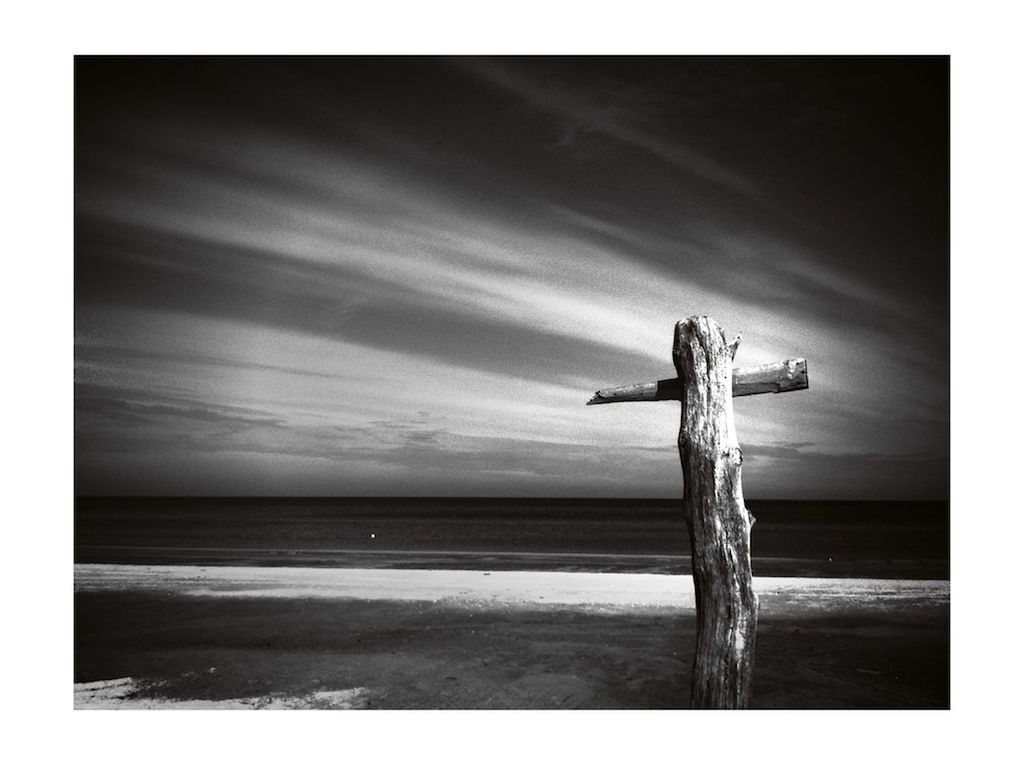 Wooden cross on calm beach against the sky