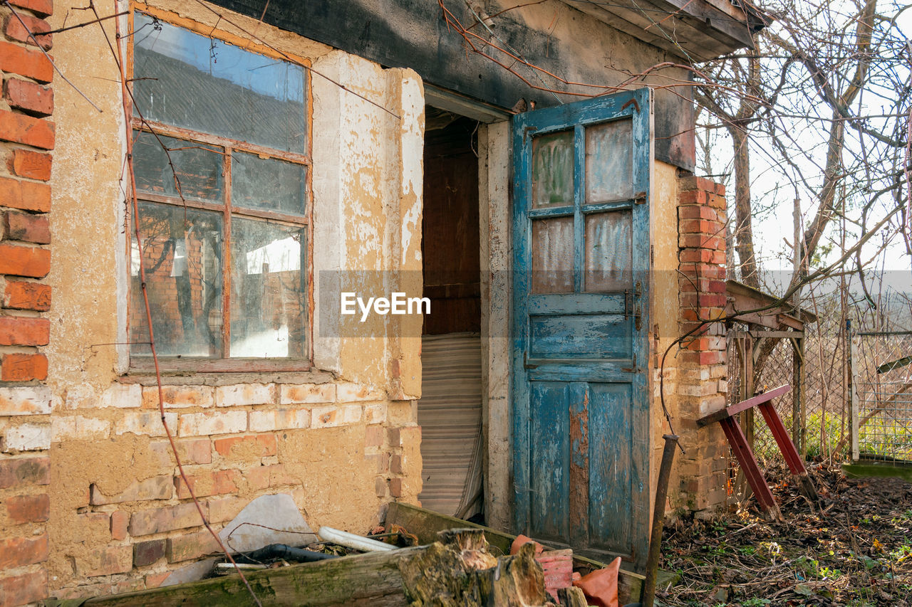 Retro-styled abandoned brick barn or farmhouse with open blue doors and big window .