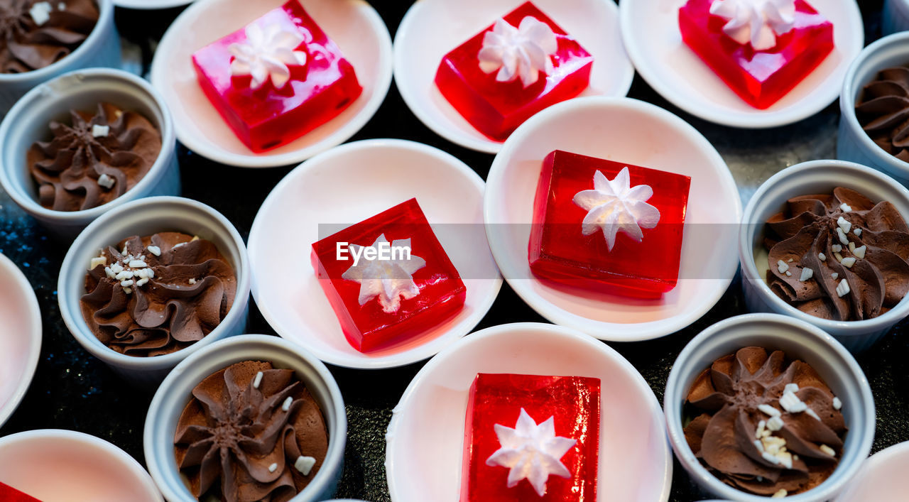 Red jelly dessert with whipped cream served on white plate and cupcakes with chocolate mousse.