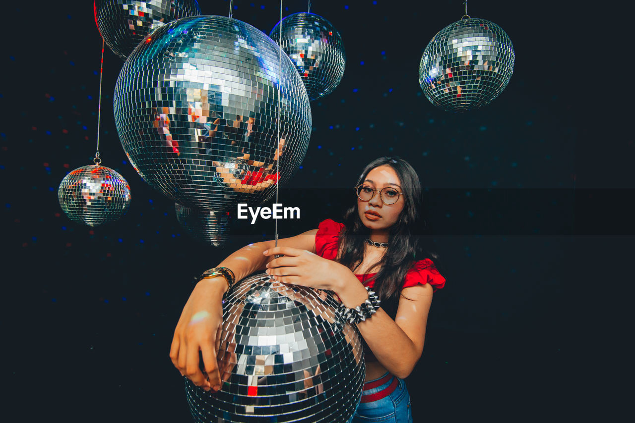 Portrait of young woman standing by disco balls in nightclub