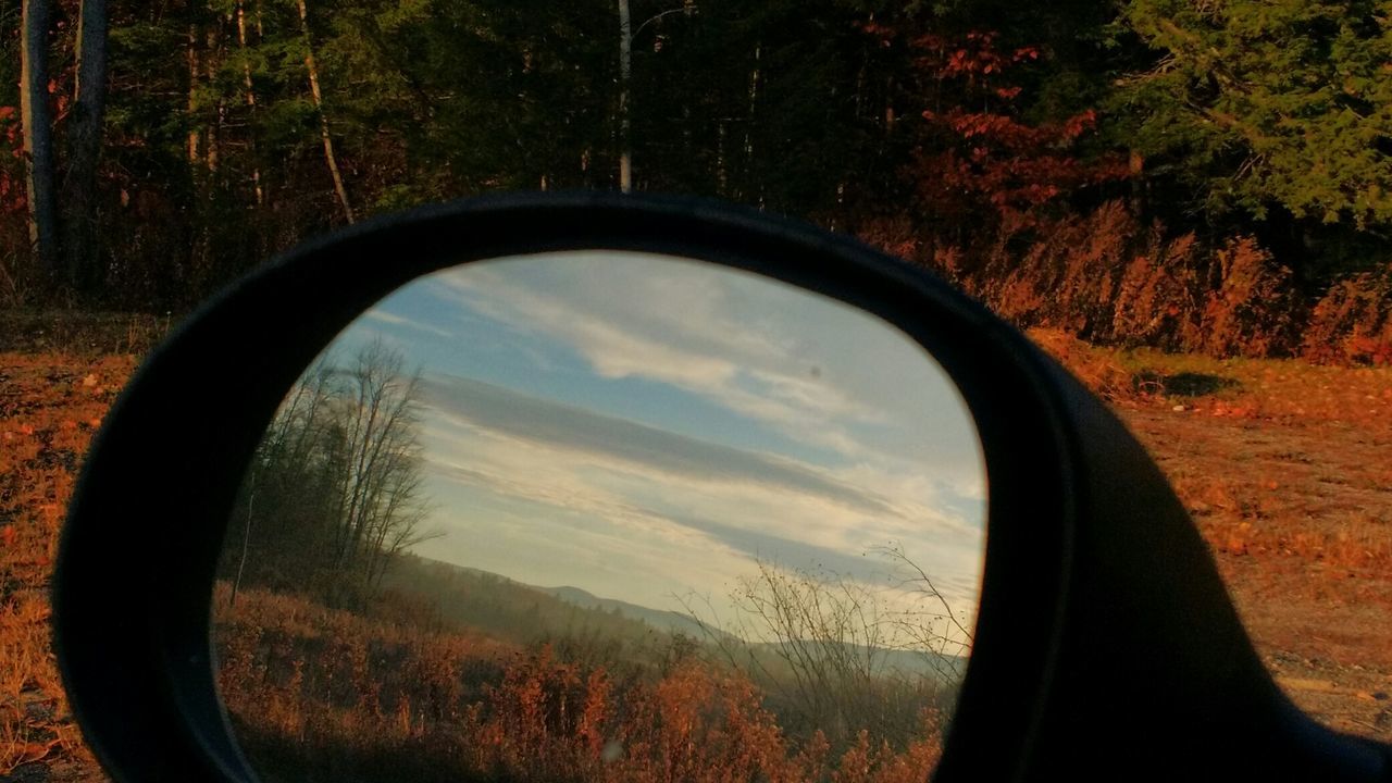 Reflection of grassy landscape on side-view car mirror during autumn