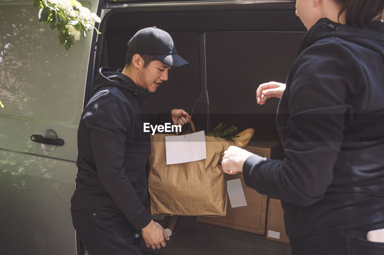 Delivery man talking to female colleague while holding package near truck