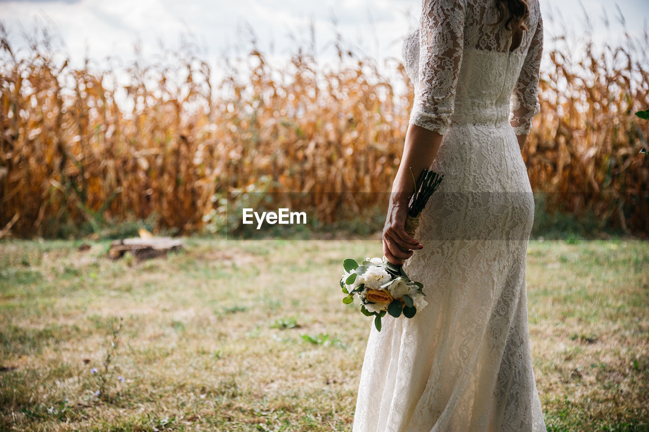 Midsection of bride holding flowers on field